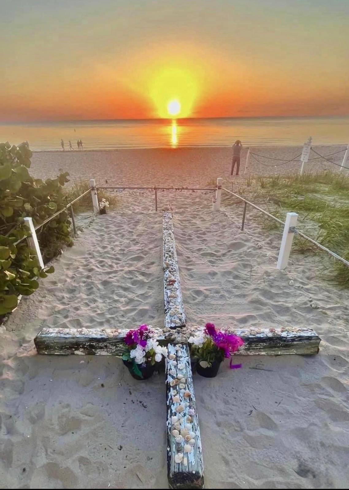 Sunrise over the Miracle Cross with fresh flowers on the sand